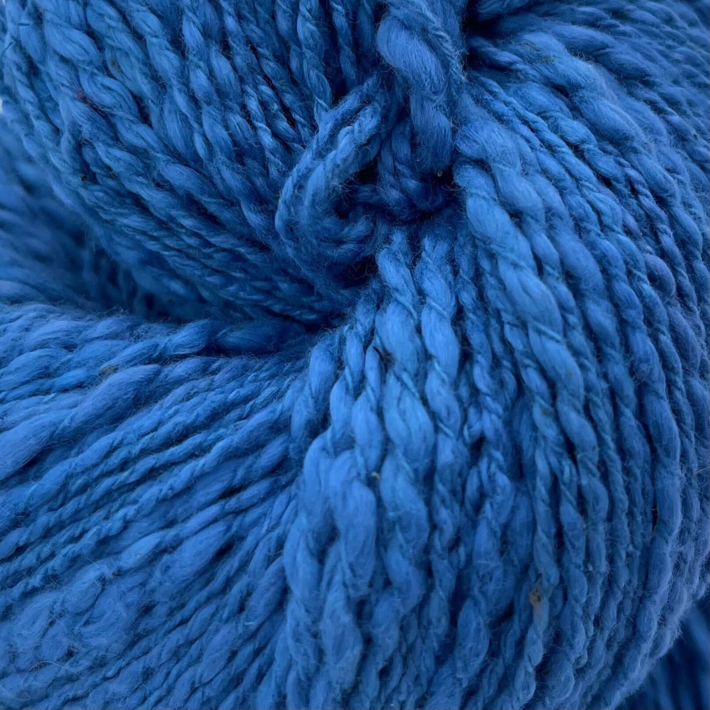 A close up of a skein of blue cotton yarn on a white background