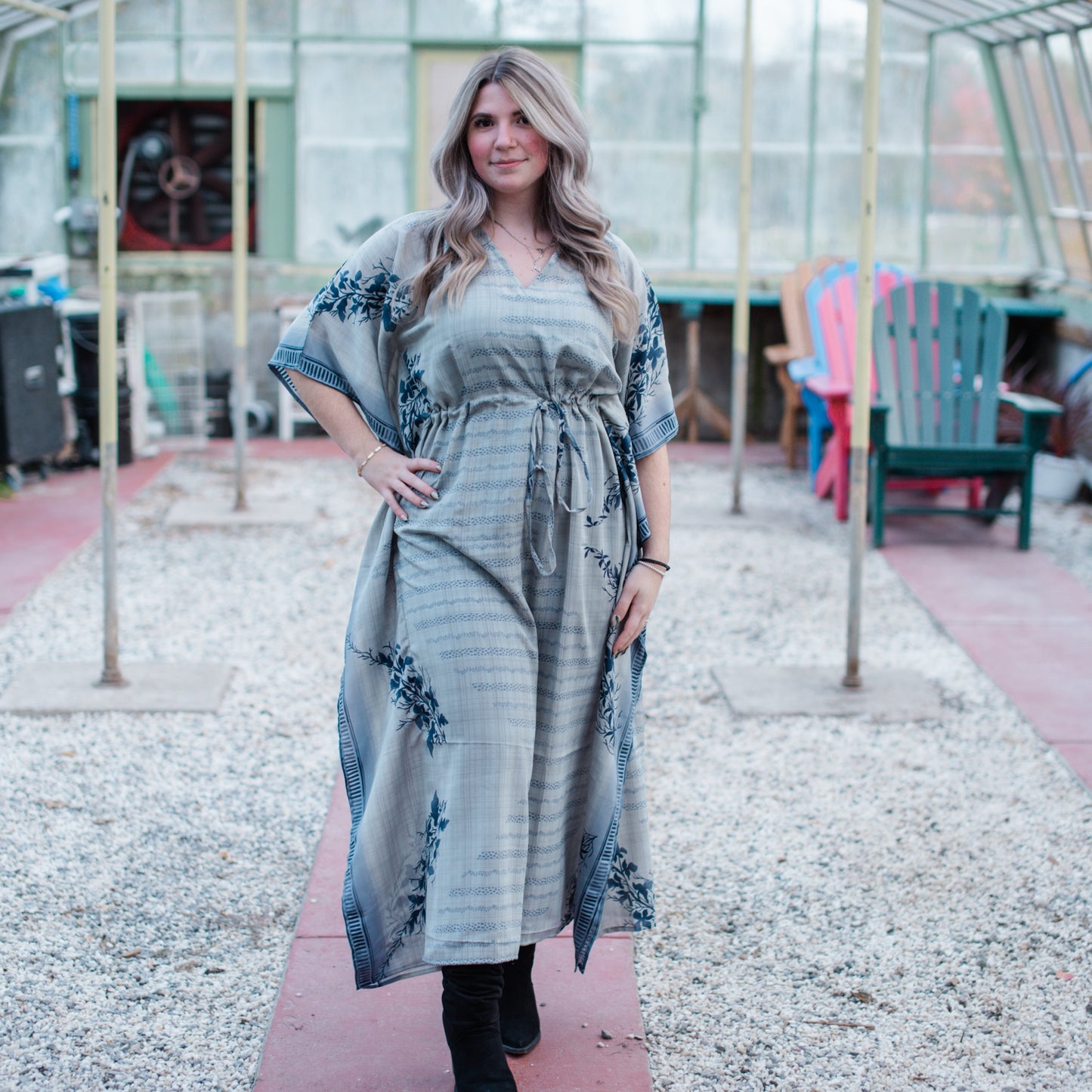 A blonde model with her hand on her hip. She's wearing a Grey Reclaimed Sari Long Kaftan with floral patterns and black boots.