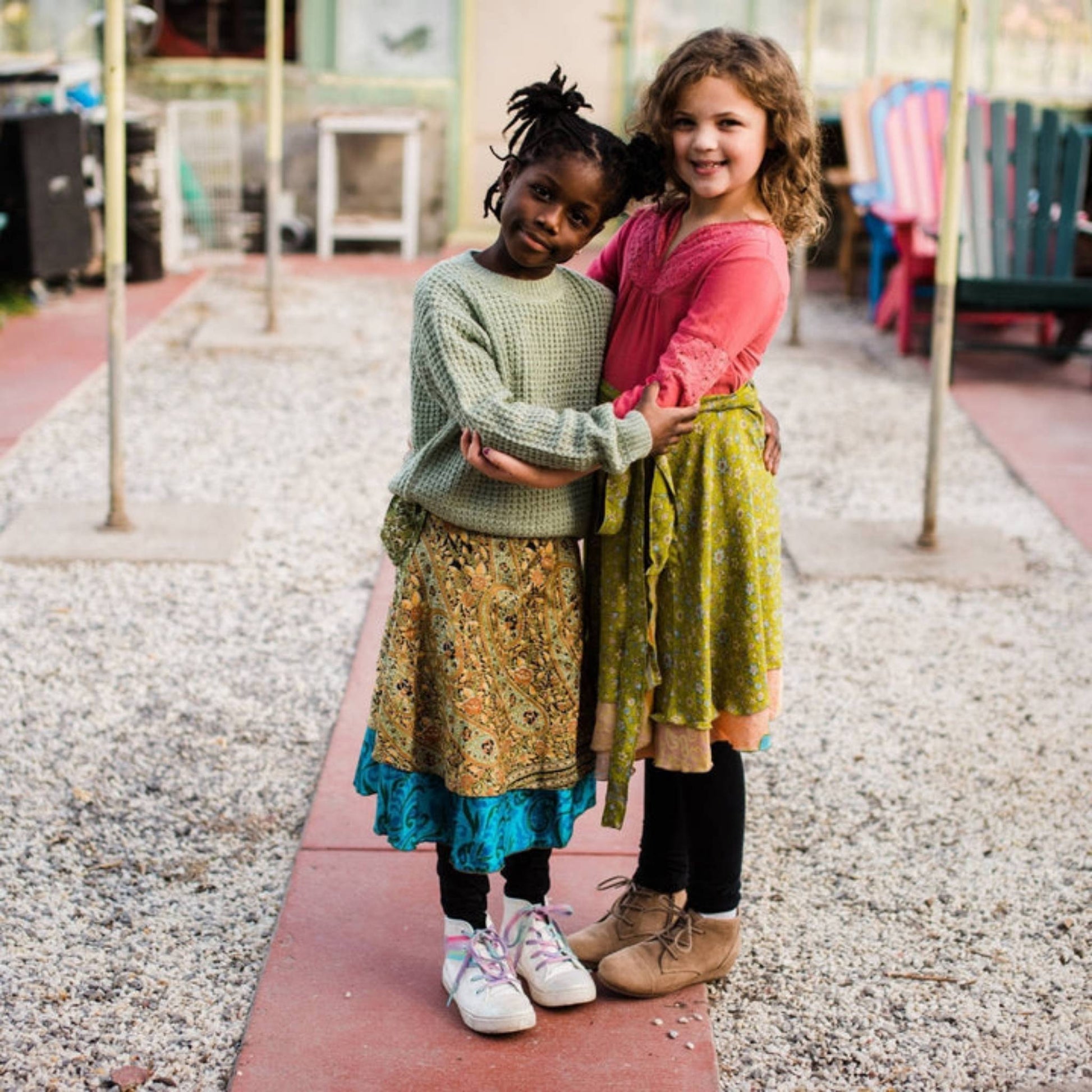 Two kid models wearing junior sari wrap skirts while standing in a greenhouse.