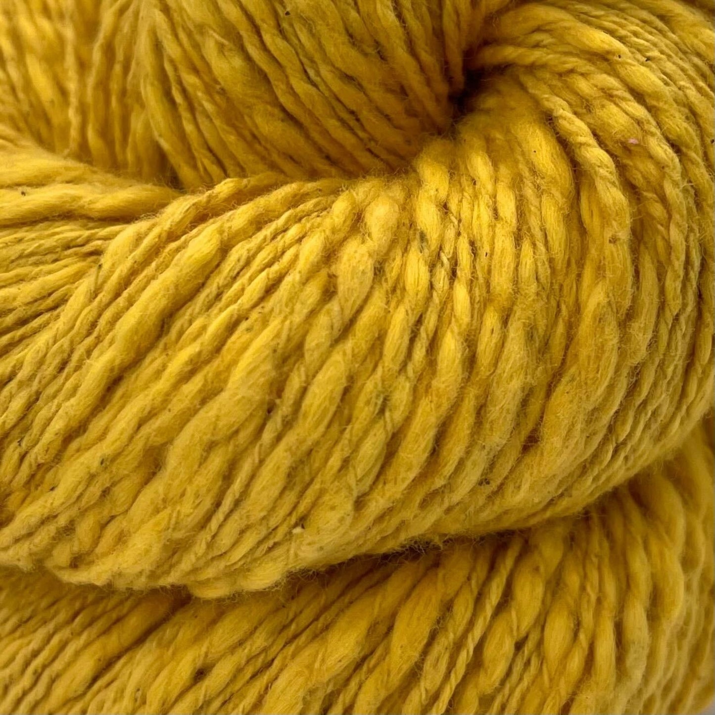 A close up of a  skein of goldenrod yellow cotton yarn on a white background