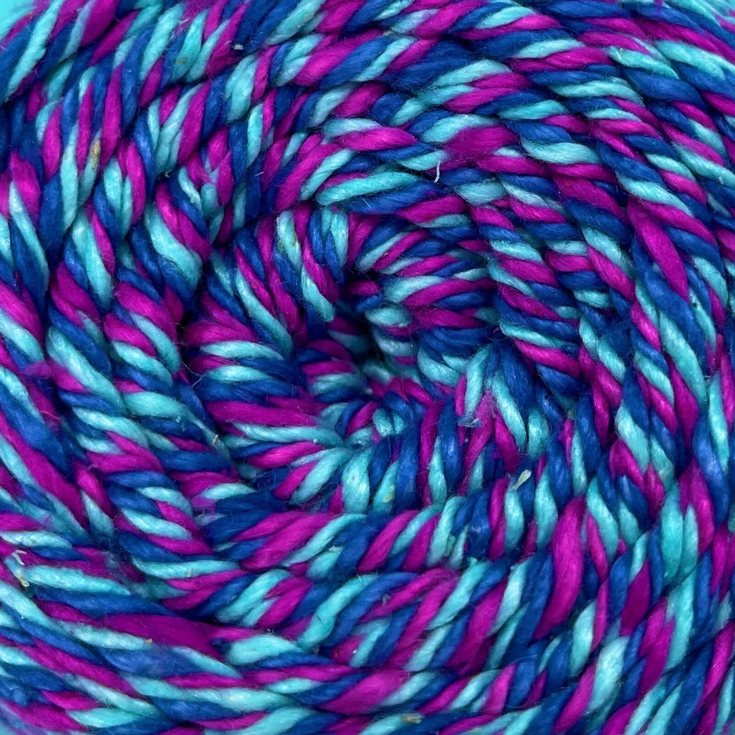 A close up of a skein of reclaimed silk yarn on a white background. The yarn is a triple ply yarn with pink, turquoise and navy colors.