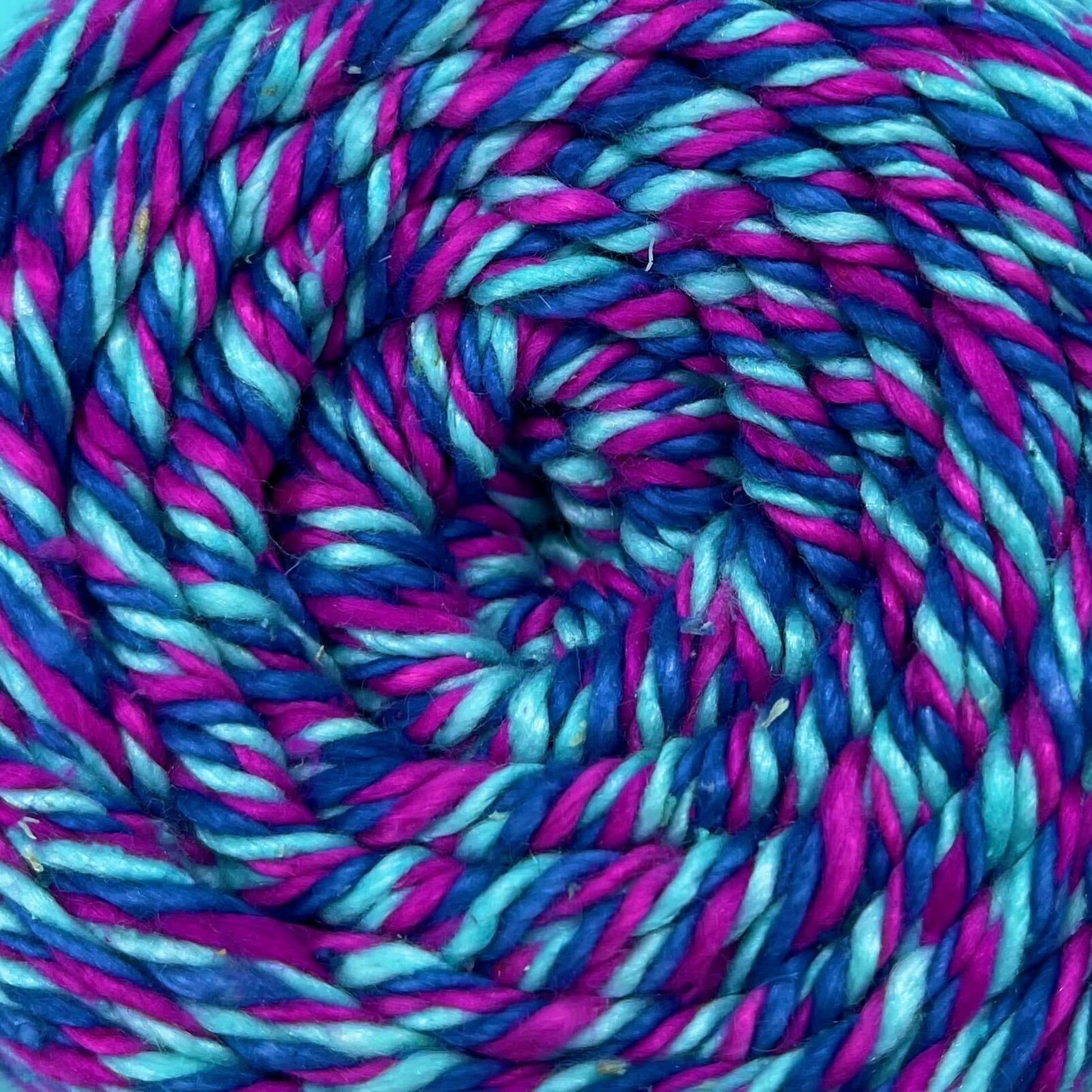 A close up of a skein of reclaimed silk yarn on a white background. The yarn is a triple ply yarn with pink, turquoise and navy colors.
