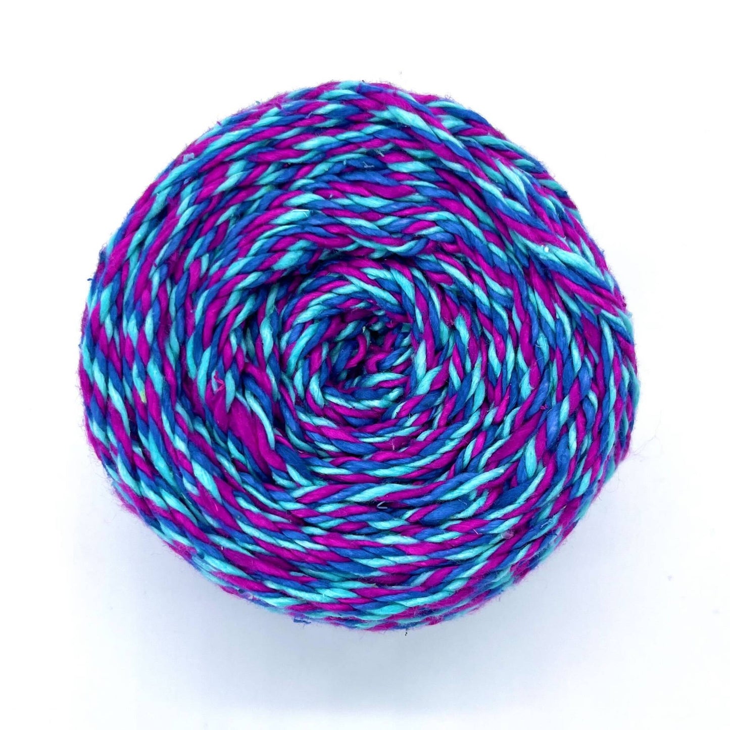 A skein of reclaimed silk yarn on a white background. The yarn is a triple ply yarn with pink, turquoise and navy colors.