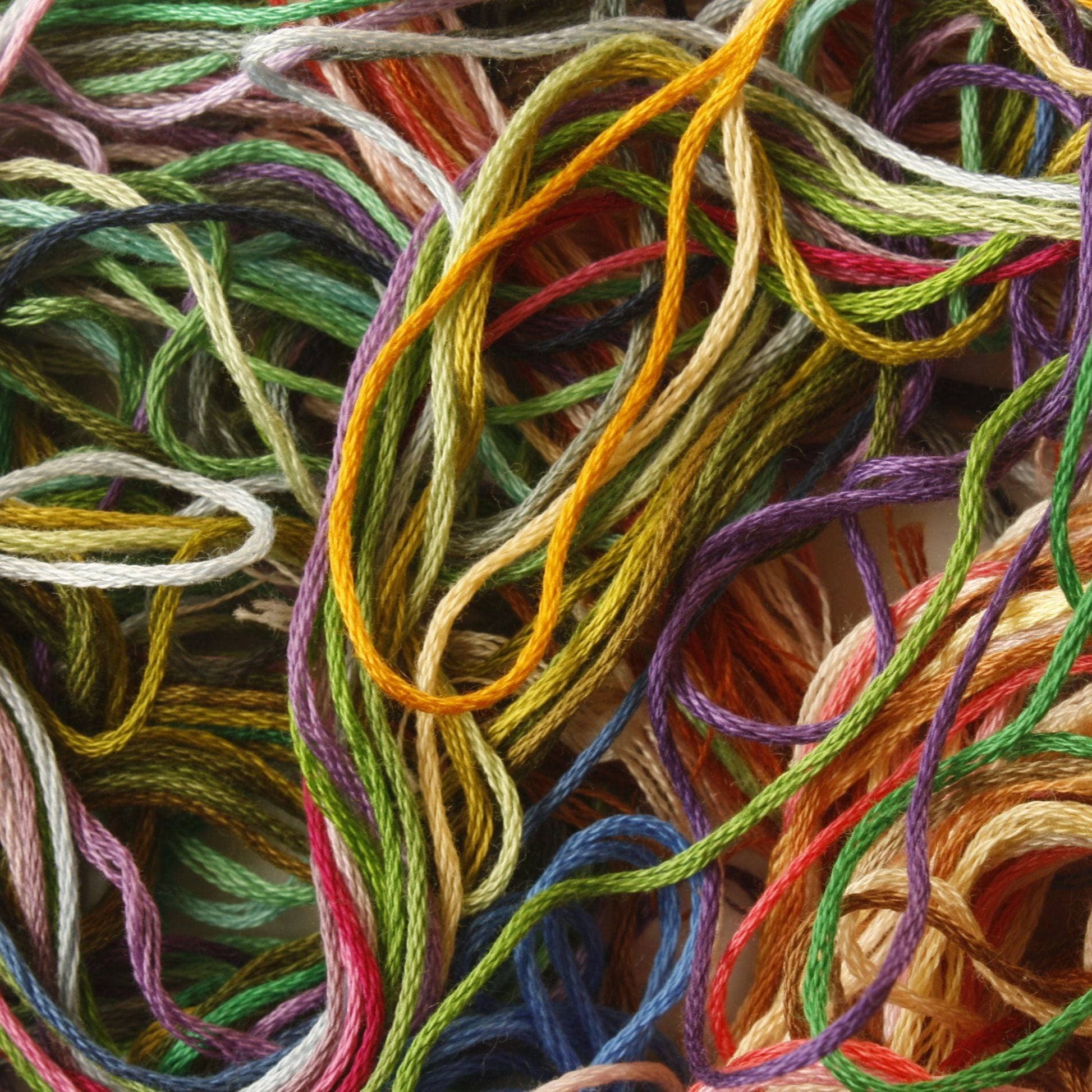 Close up view of assorted colorful yarn threads. Yellow, green, blue, red, pink, peach, magenta, and beige.