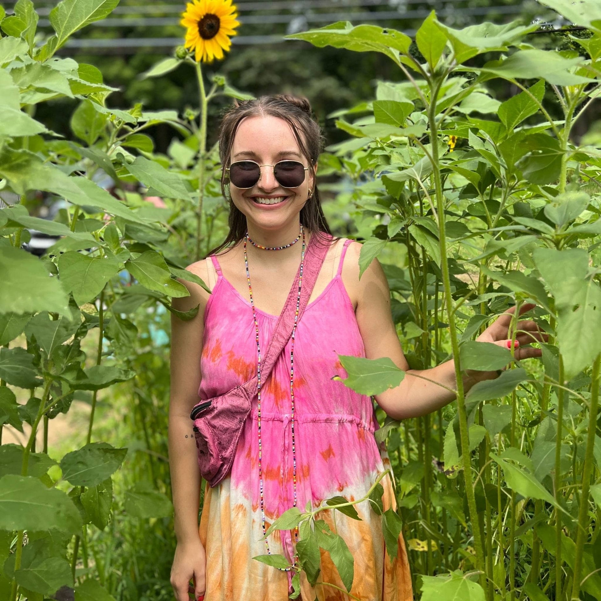 Model is walking through a sunflower field wearing the rainbow sherbet tie dye maxi dress.