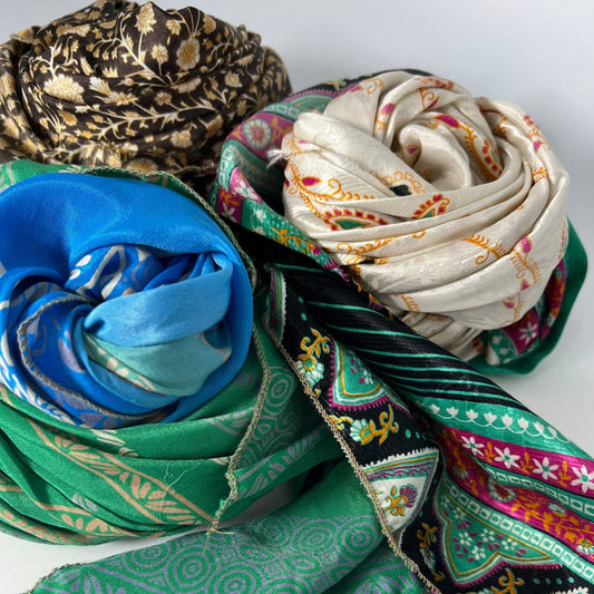 Three pieces of sari silk fabric in various colors all rolled up in a ball on a white backdrop.