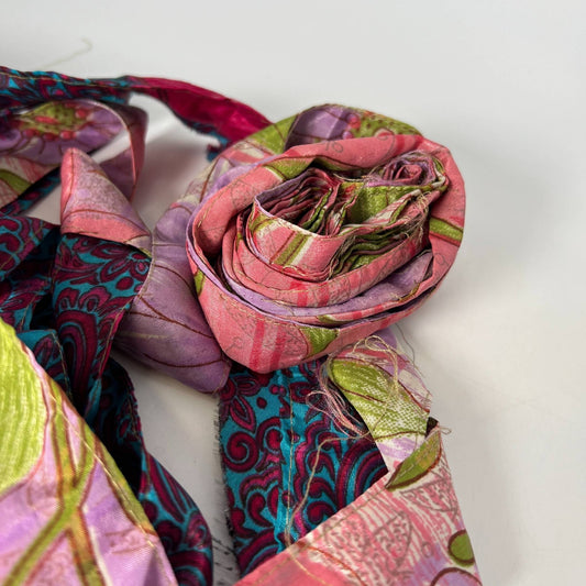 A pink piece of sari silk fabric rolled up on a white backdrop.