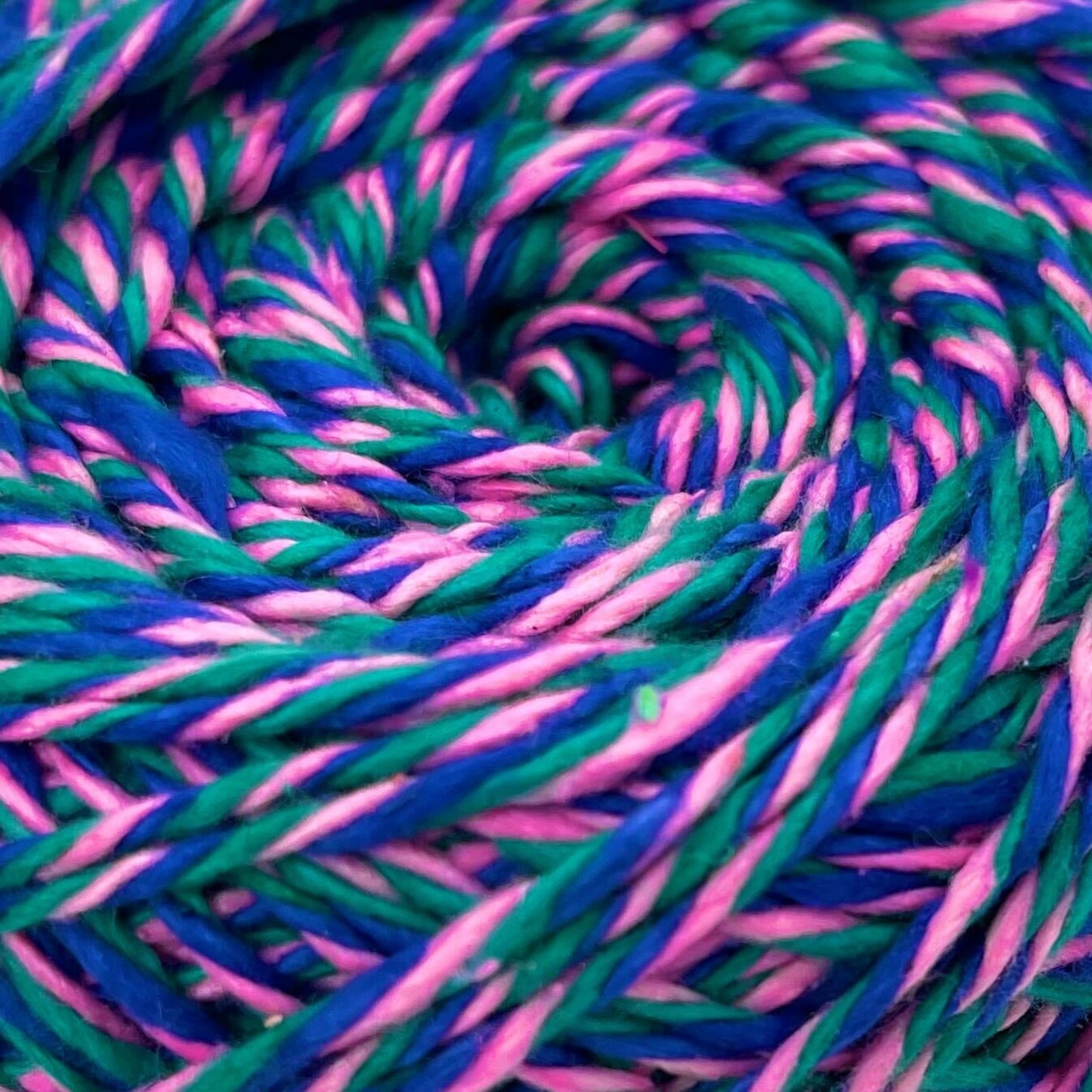 a close up a skein of reclaimed silk yarn on a white background. The yarn is a triple ply yarn with pink, green and navy colors.