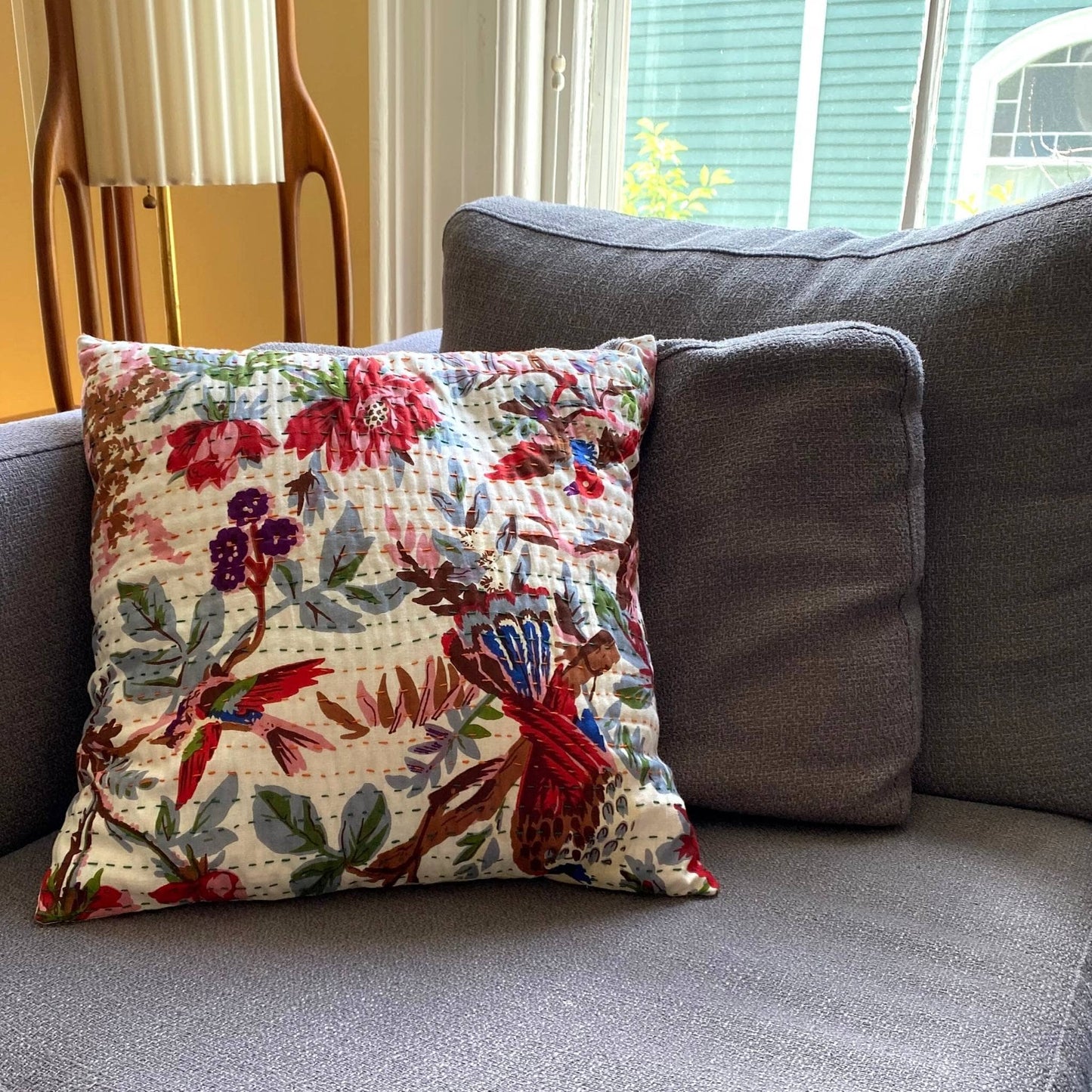 Vibrant Rainforest kantha pillow laying on a grey couch.