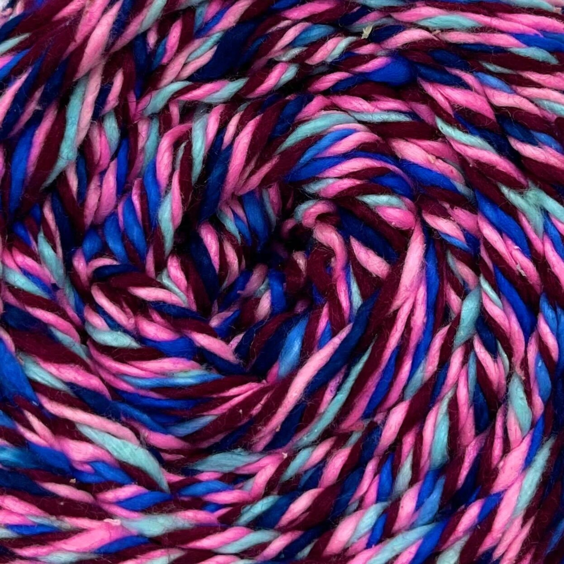 A close up of a skein of reclaimed silk yarn on a white background. The yarn is a triple ply yarn with dark plum, pink, turquoise navy and cobalt blue colors. 