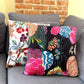 One vibrant rainforest and one night lily kantha pillow sitting on a grey couch.