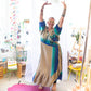 Model has their hands up above their head wearing a beige and blue zaria wrap dress while standing in a a bright room. 