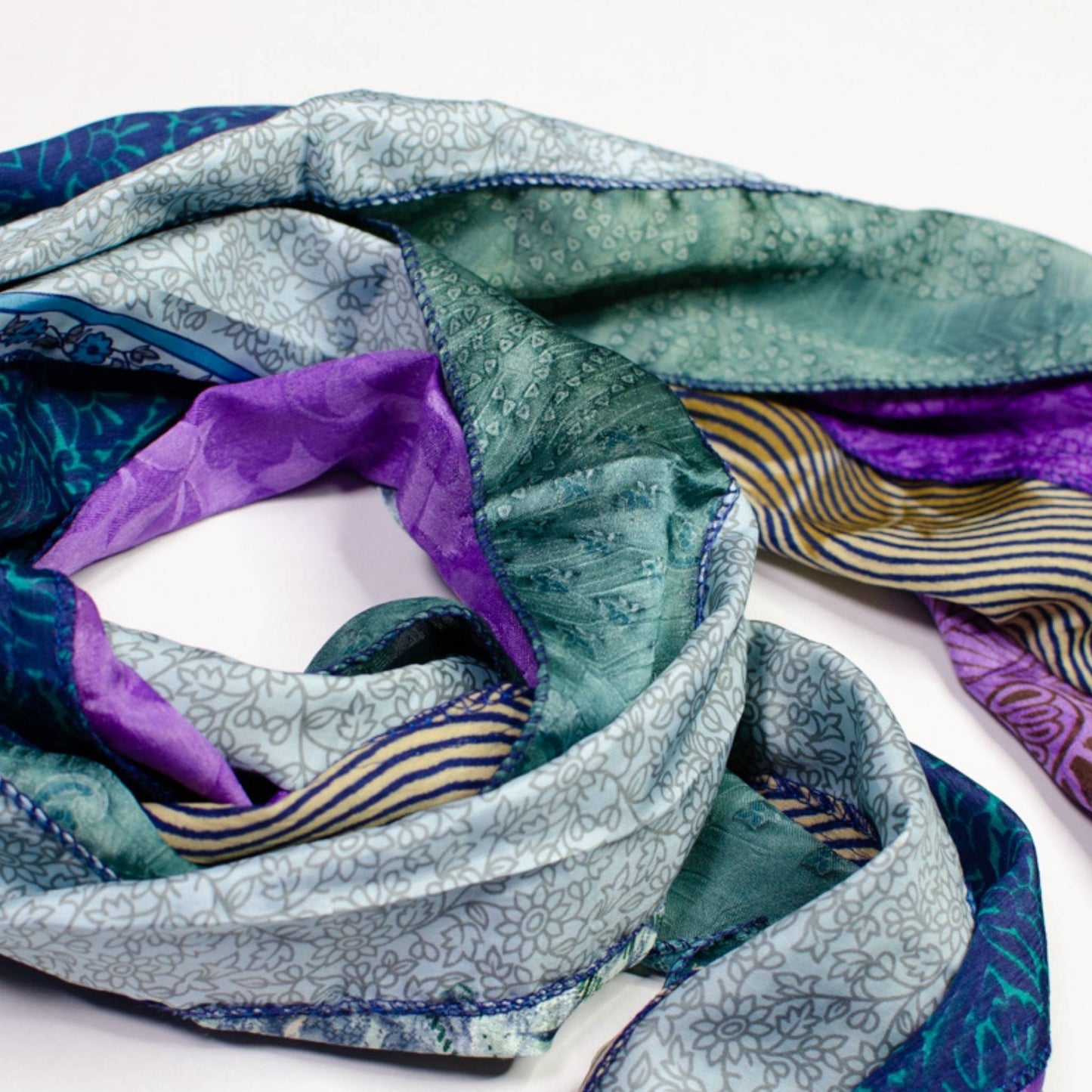 Blue, green and purple medley scarf rolled up on a white backdrop.