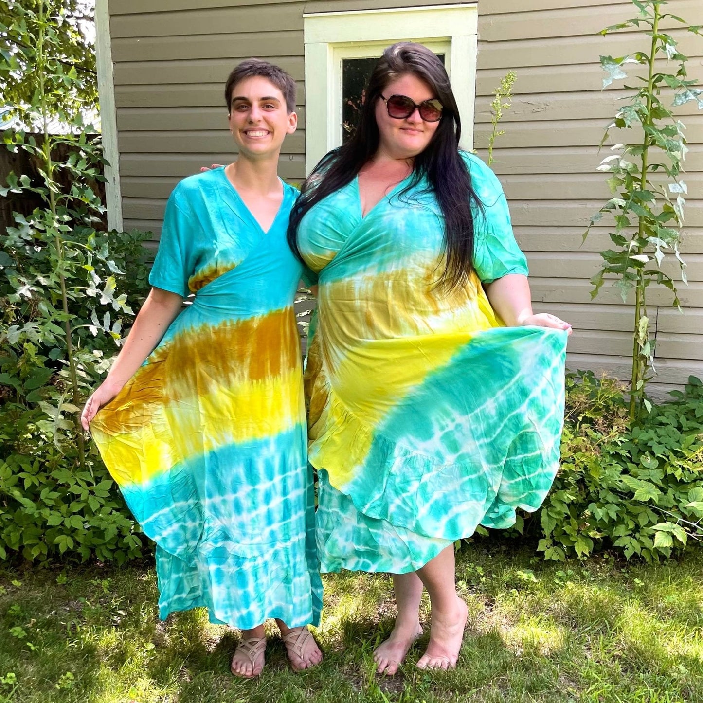 Two models standing outside in front of a shed wearing womens and goddess size tie-dye wrap dresses.