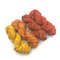 Chiffon Ribbon yarn is the colorway Bonfire on a white background. These colors are warm oranges and yellows.