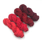 Chiffon Ribbon yarn is the colorway Lava on a white background. These colors are light reds to dark maroons.