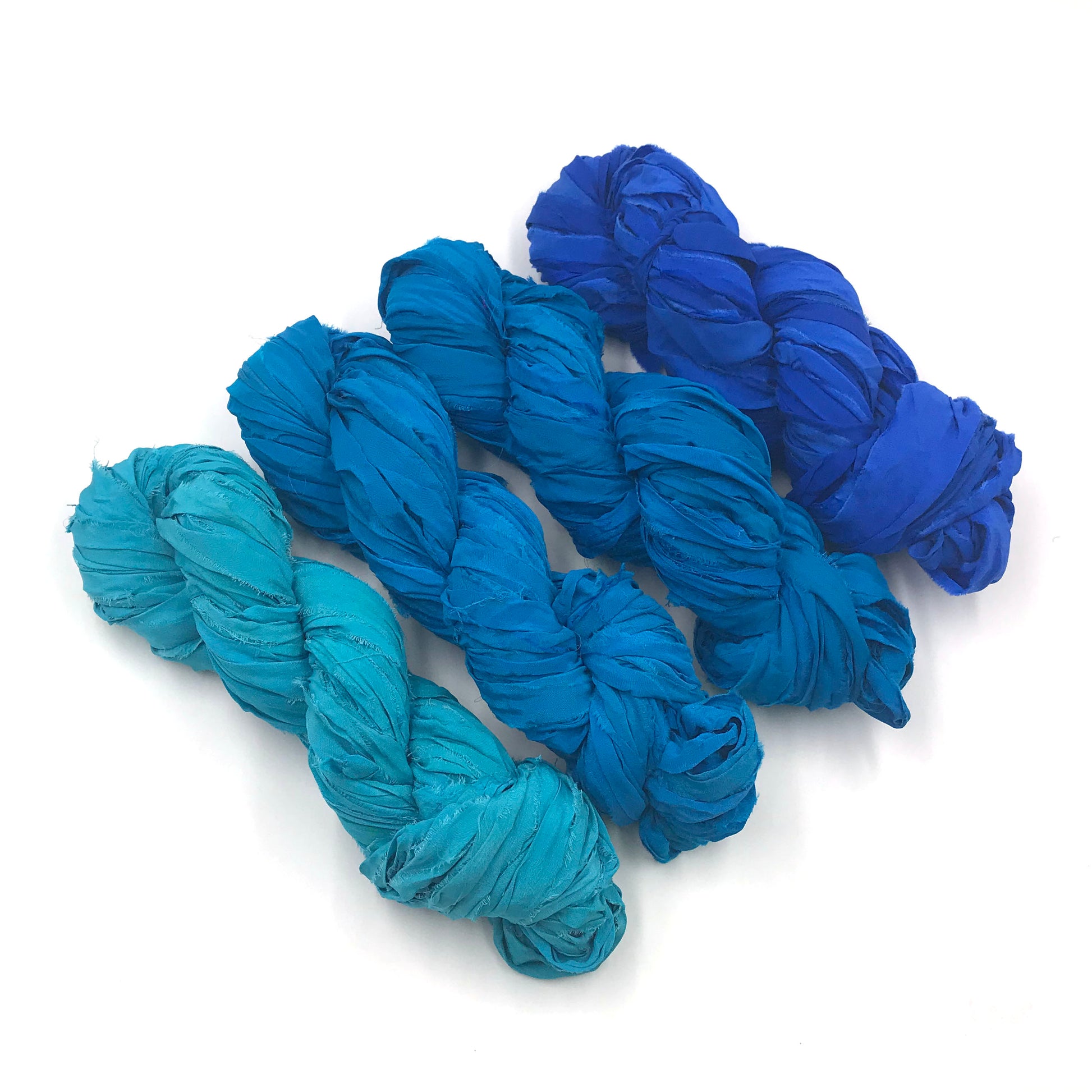 Chiffon Ribbon yarn is the colorway Ocean Waves on a white background. These colors are light aqua to deep blue.