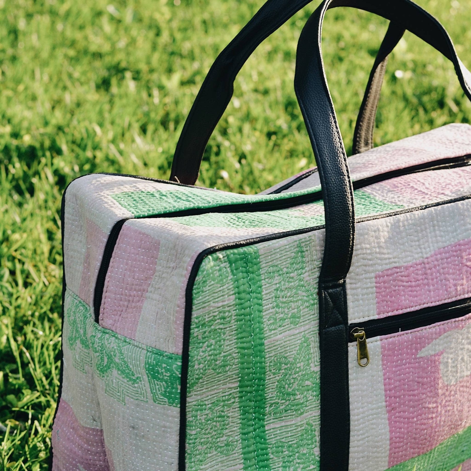 Close-up of green and pink kantha duffle bag sitting in the grass. 