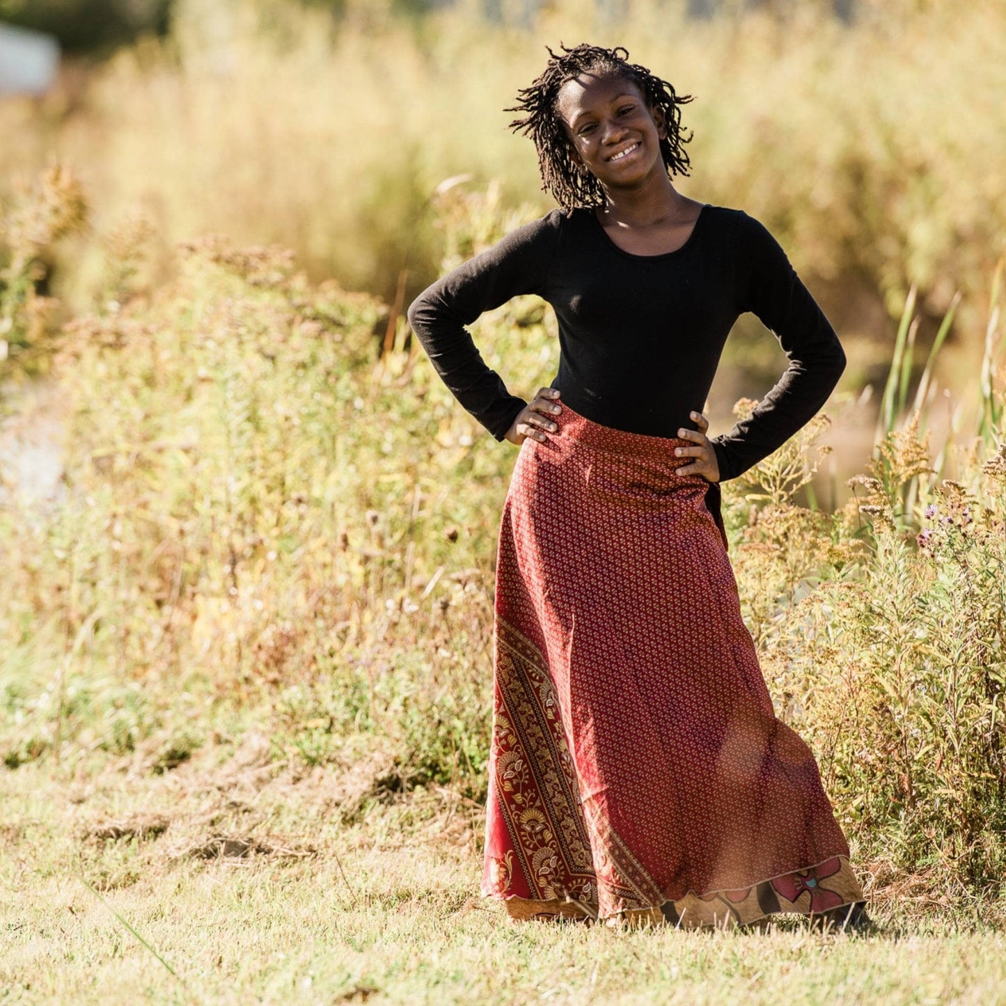 Junior model wearing a red maxi sari wrap skirt in a field. 
