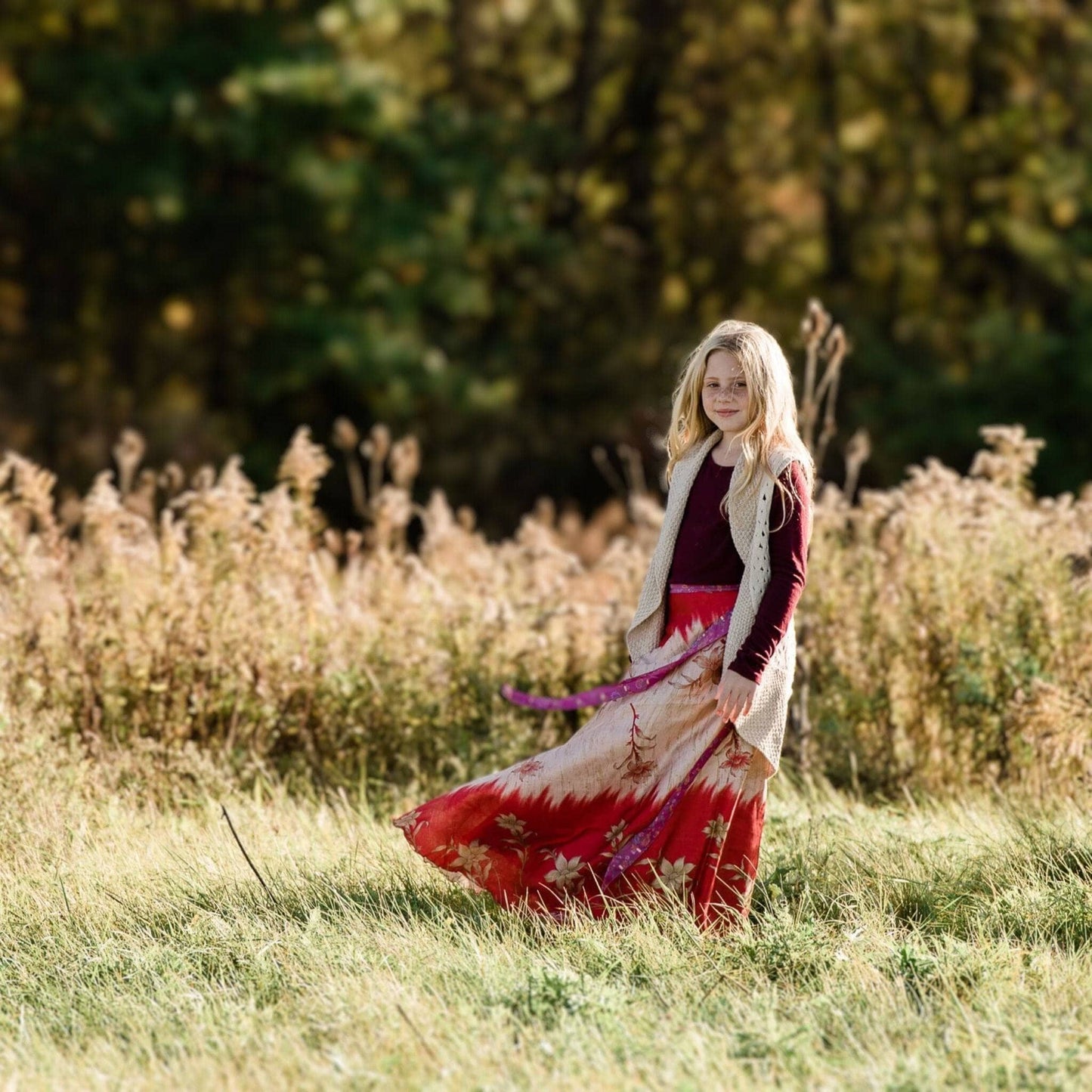 Model is standing in a grassy field wearing a juniors red tie dye sari wrap skirt. 