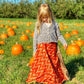 Kid model walking through a field of pumpkins wearing a  maxi sari wrap skirt in orange. 