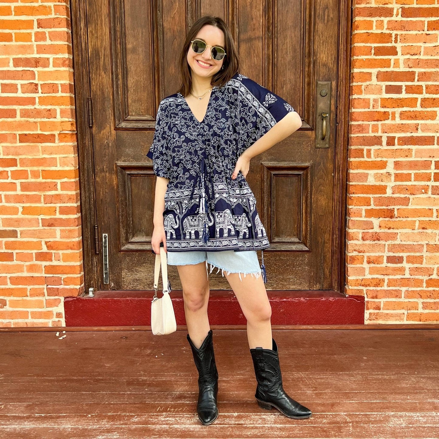 Model is wearing a navy eloise kaftan while standing in front of a wooden door on a brick porch.