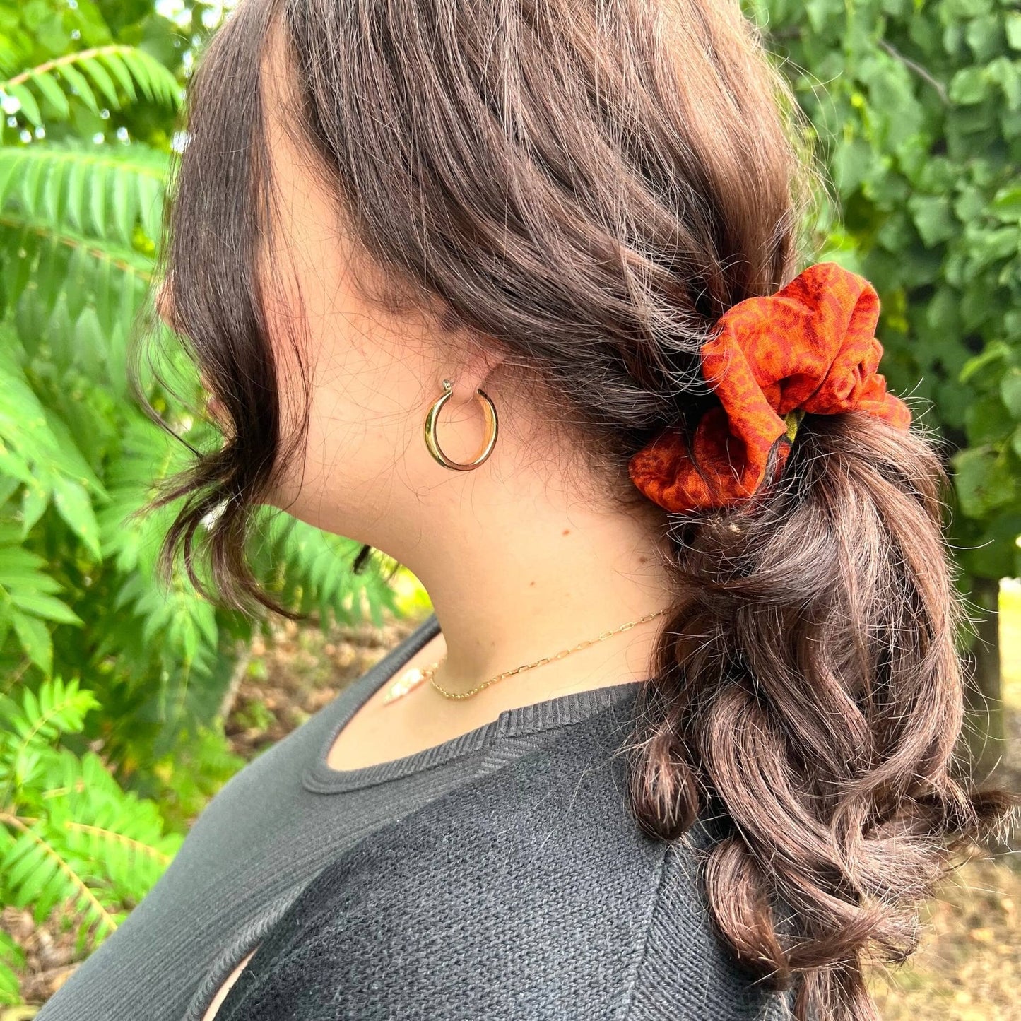 Model has their hair tie up in a ponytail wearing an orange sari silk scrunchie.
