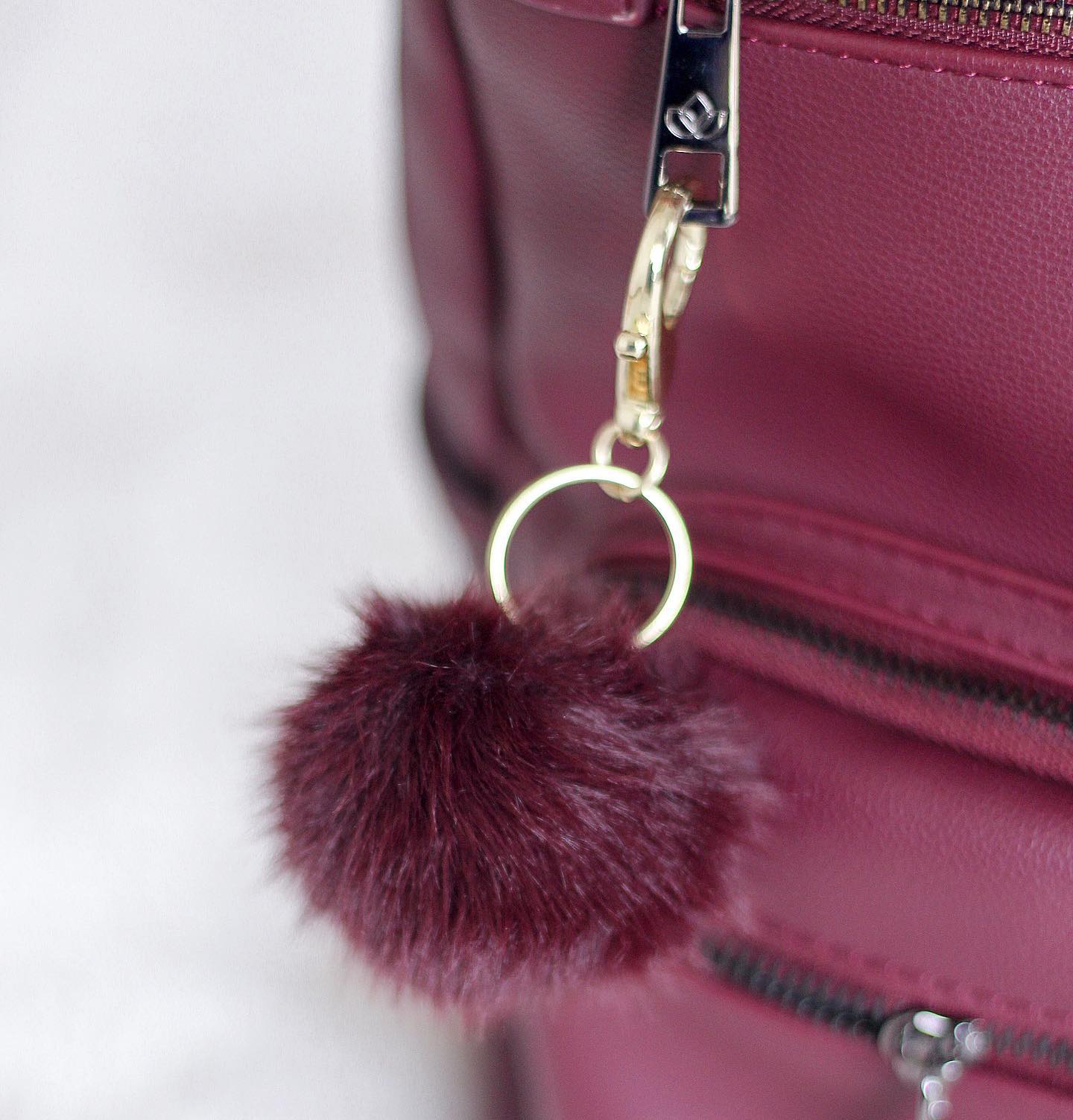 completed pom pom kit keychain attached to red purse in front of a white background.