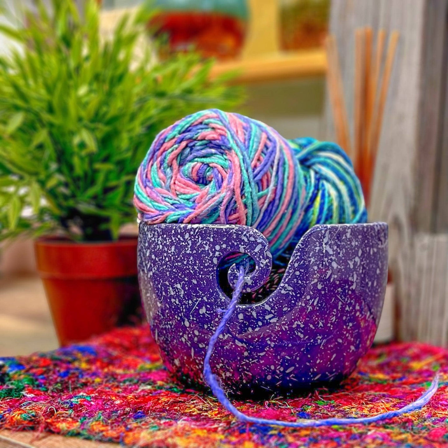 Purple speckled yarn bowl with three colorful skeins in it. A plant and incense can be seen in the background.