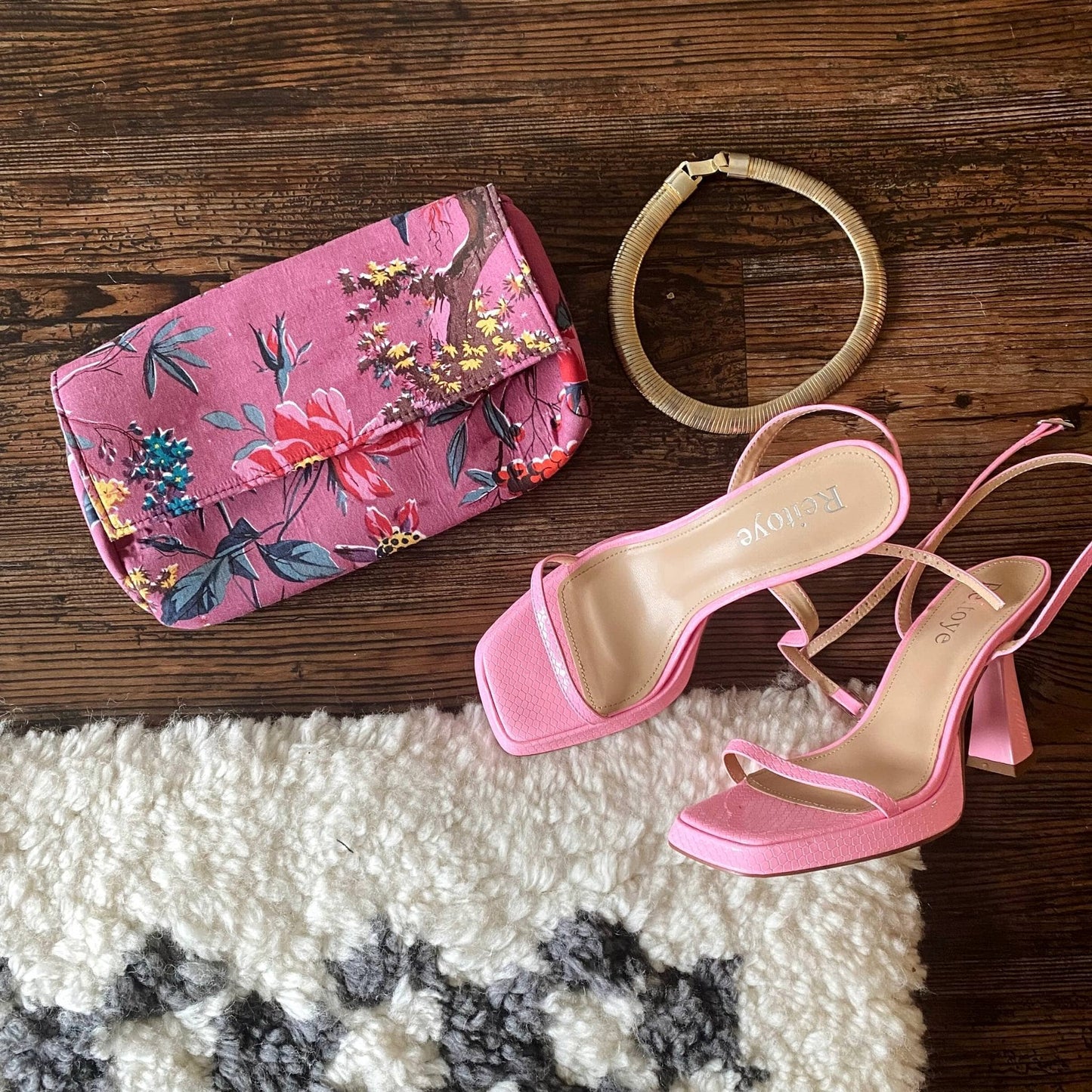 A purple cotton clutch is laying on the floor with some high heels and a necklace.