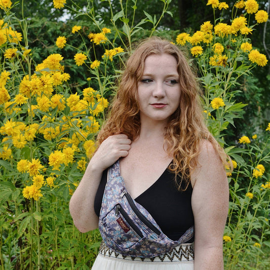 model wearing purple floral fanny pack in front of yellow flowers