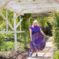 Model is standing outside under a wooden pergola wearing a purple sedona patchwork skirt as a dress.