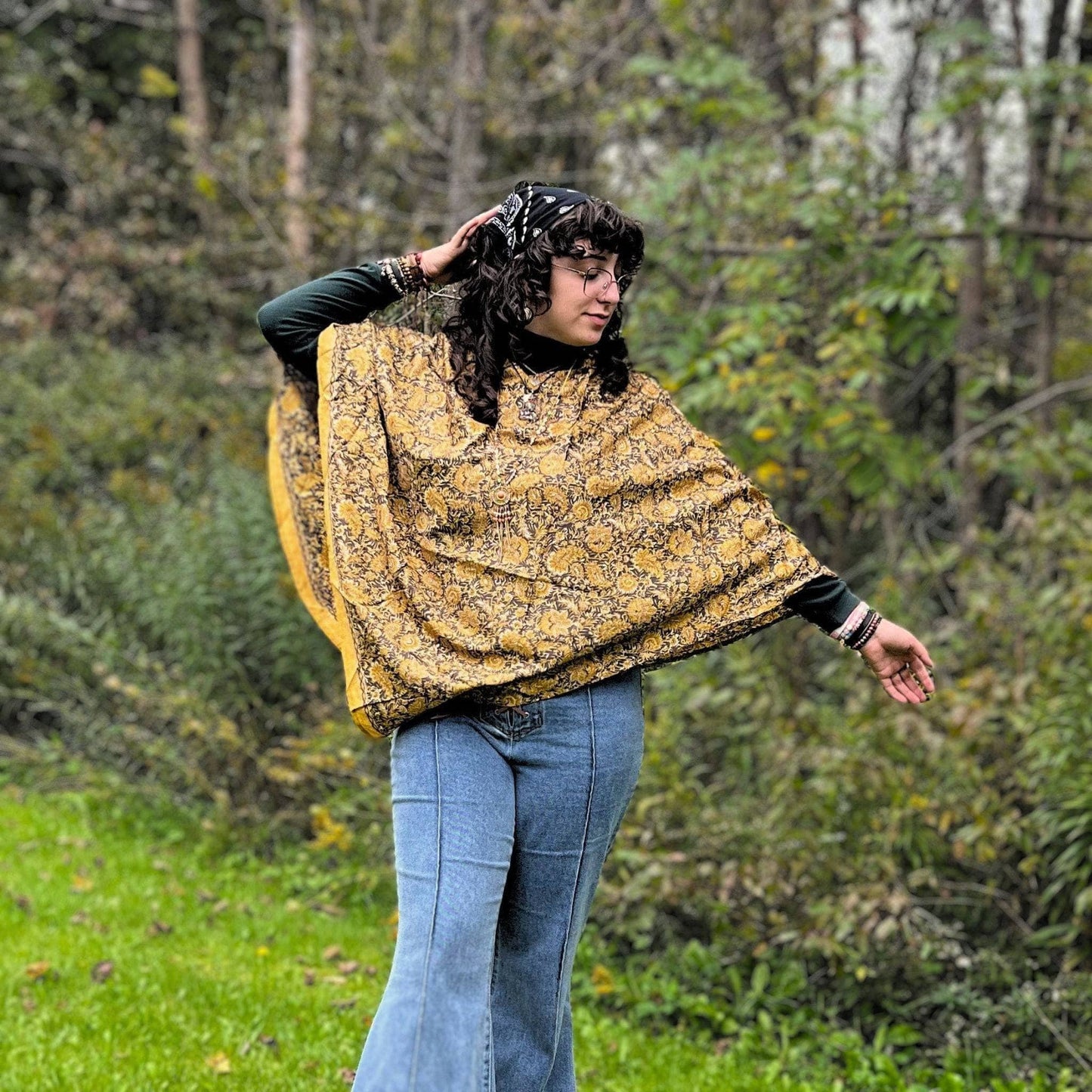 A girl standing in a field wearing denim bell bottoms and a mustard yellow recycled sari hooded poncho