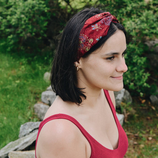 Model is wearing a red kameela knot headband while standing outside. 