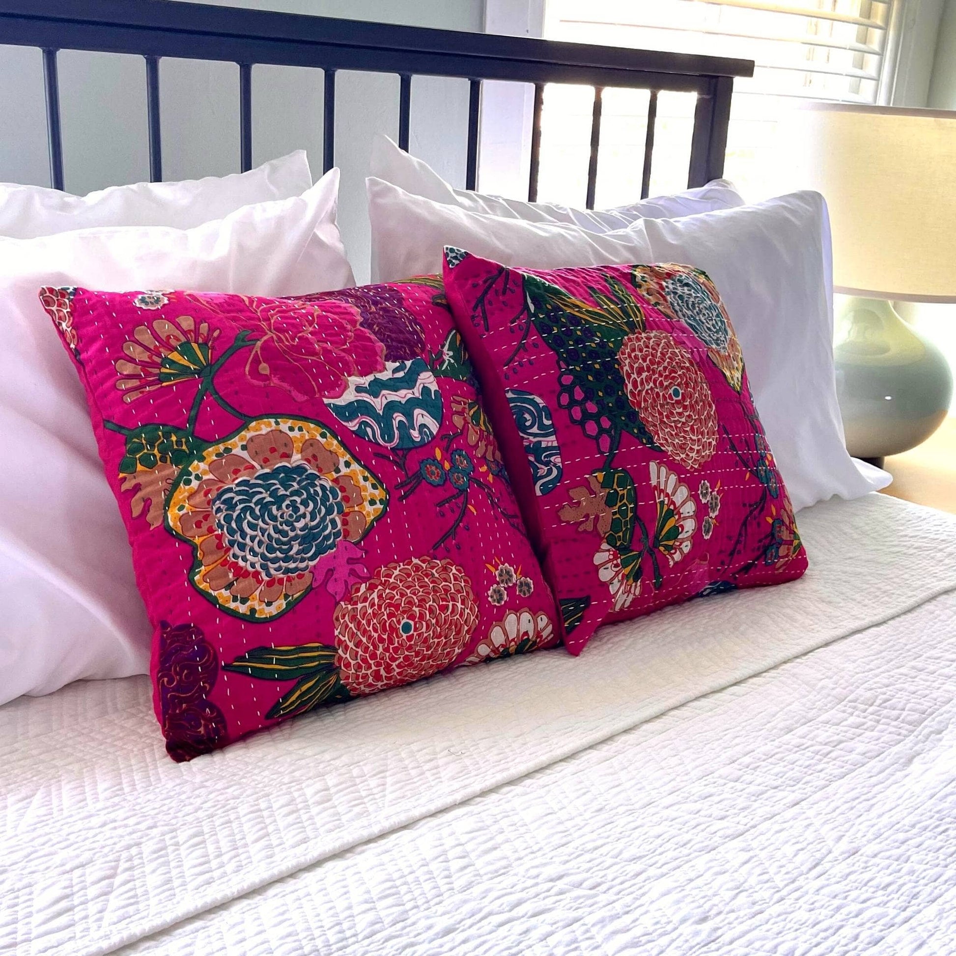 Matching set of pink kantha pillow covers in a bed with a white comforters.