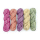Chiffon Ribbon yarn is the colorway Vintage Chic on a white background. These colors are light blush pink, pea green, light yellow, orange and purple