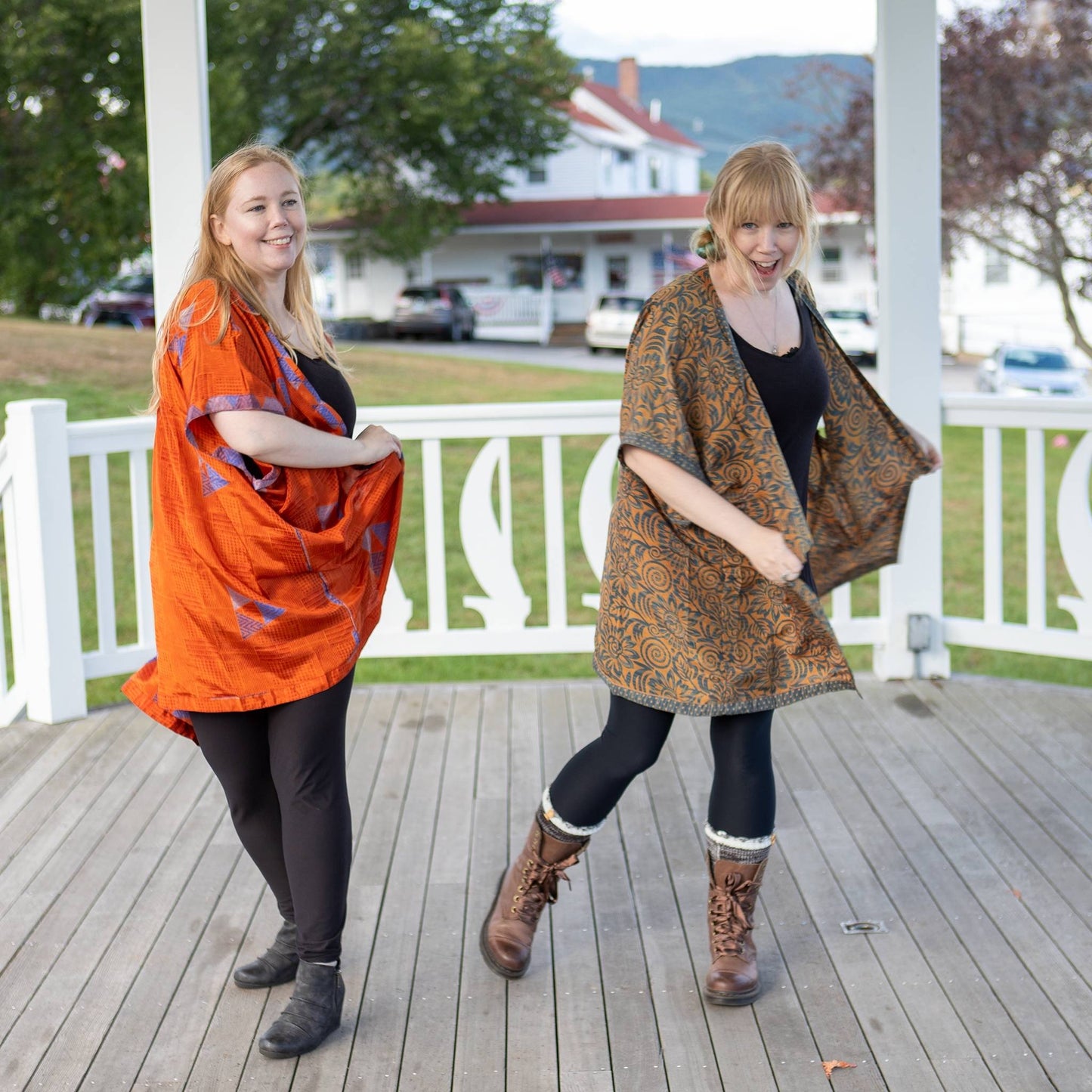 Two models are twirling on a white pergola outside wearing fall tone amara short dusters. 